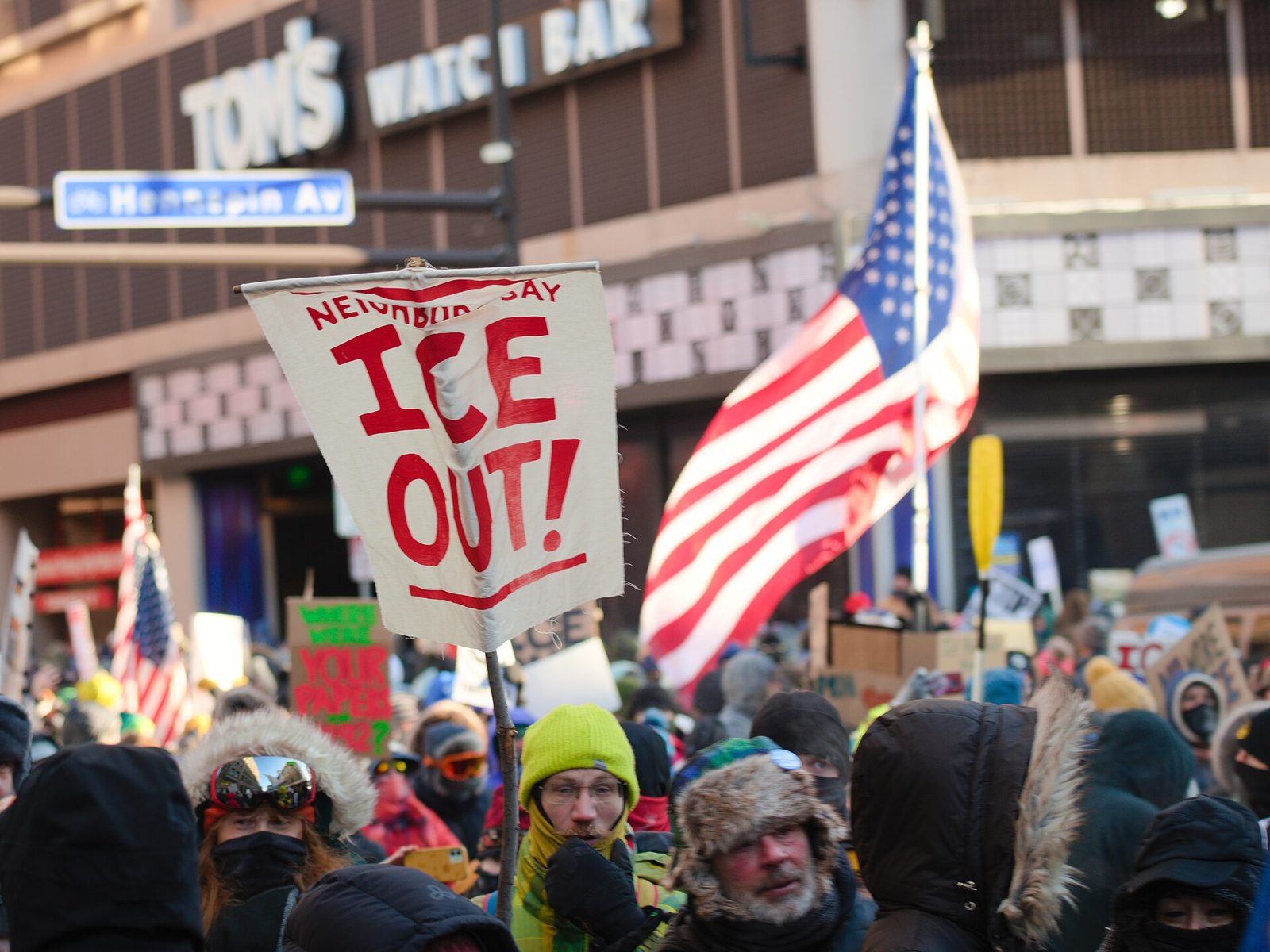 Protesta contra ICE con un cartel que dice ICE OUT y una bandera de EE.UU.